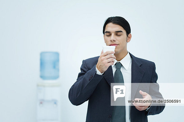 Businessman holding and smelling disposable cup with eyes closed  water cooler in background