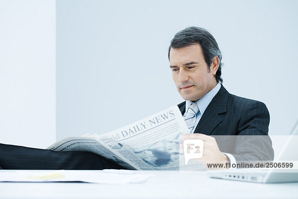 Geschäftsmann am Schreibtisch sitzend  Zeitung lesend  mit besorgter Miene nach unten schauend
