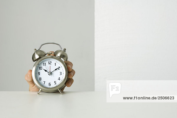 Old-fashioned alarm clock  hand reaching up to grab it from behind