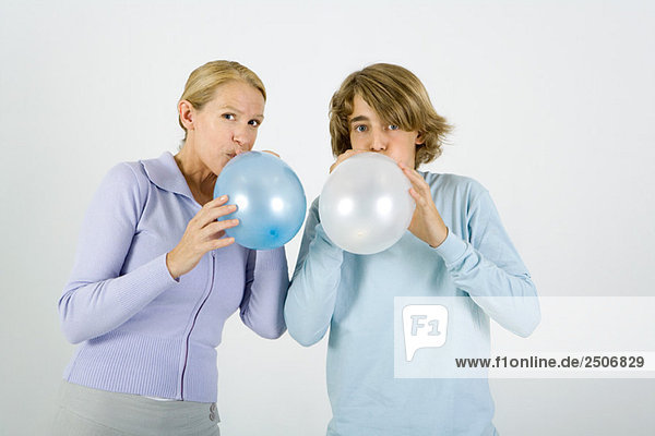Mutter und jugendlicher Sohn stehen Seite an Seite  Luftballons aufblasen  in die Kamera schauen