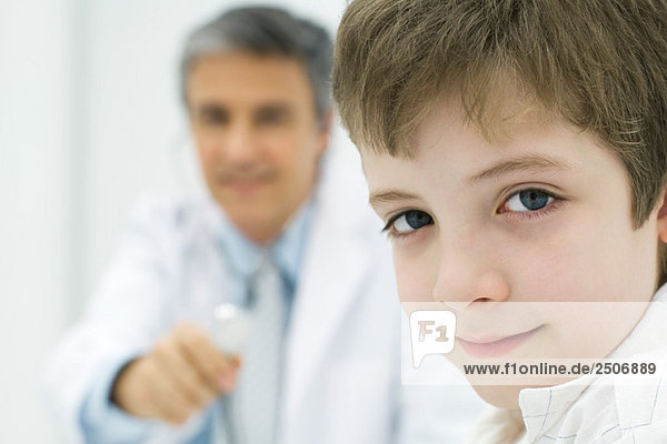 Junge lächelt in die Kamera  Arzt hält Stethoskop im Hintergrund