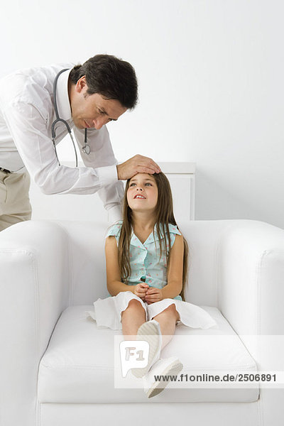 Männlicher Arzt  der die Stirn eines jungen Patienten fühlt  Mädchen  das auf einem Sessel sitzt.