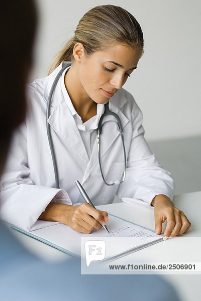 Arzt schreibt am Schreibtisch  Patient im Vordergrund