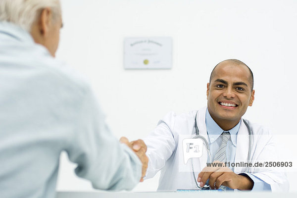 Arzt schüttelt sich die Hände mit dem Patienten  lächelt in die Kamera  abgeschnitten