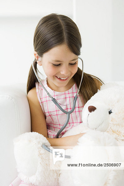 Mädchen hört Teddybärherz mit Stethoskop