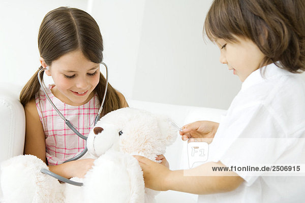 Zwei Kinder spielen Arzt  Mädchen hört Teddybärenherz mit Stethoskop