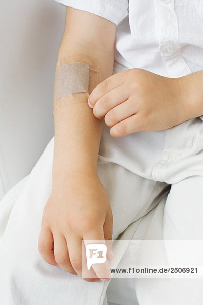 Little boy picking at adhesive bandage on his arm  cropped view
