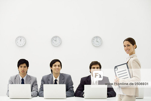 Professionelle Männer sitzen mit Laptop-Computern unter Wanduhren  Supervisorin lächelt vor der Kamera