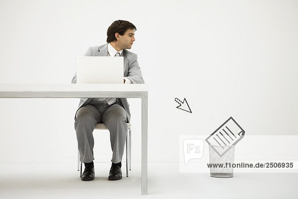 Geschäftsmann sitzt am Schreibtisch und schaut auf den Computer-Cursor  der auf ein Dokument im Mülleimer zeigt.