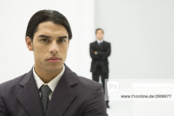 Junger Geschäftsmann mit Blick auf Kamera  Portrait  Chef im Hintergrund