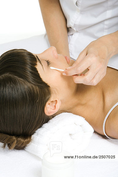 Frau liegt auf dem Rücken  Kosmetikerin reibt Wattestäbchen unter dem Auge