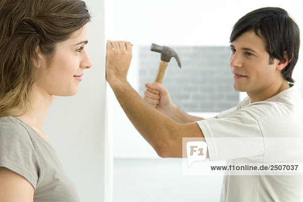 Couple smiling at each other  man hammering nail into wall