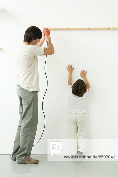 Man drilling into wall  his son reaching up  trying to help