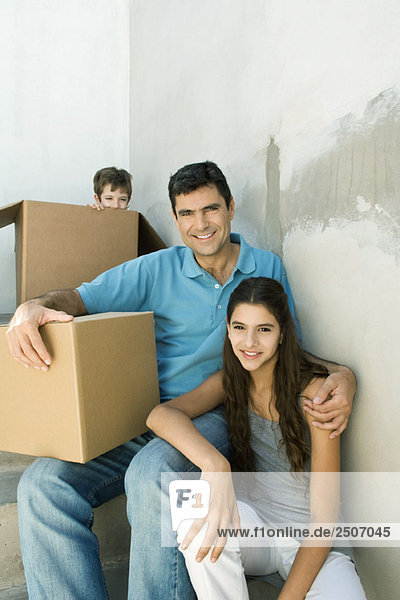 Vater und Teenagertochter im Treppenhaus mit Pappkartons  Junge versteckt im Hintergrund