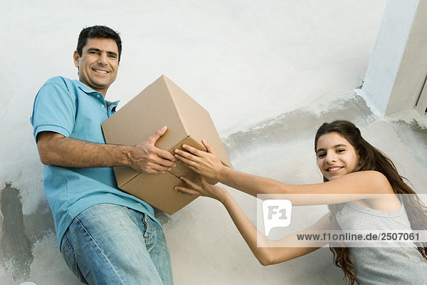 Vater und Tochter bewegen Pappkarton zusammen  Blickwinkel niedrig