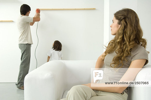 Man using drill to attach wood to wall  woman in foreground watching over her shoulder