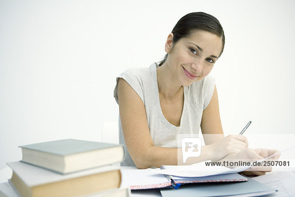 Frau arbeitet am Tisch  hält Stift und Papier  lächelt in der Kamera