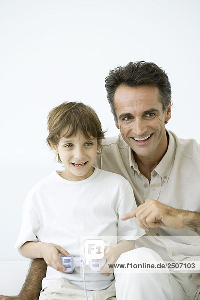 Junge spielt Videospiel  Vater sitzt mit ihm  zeigt auf Controller