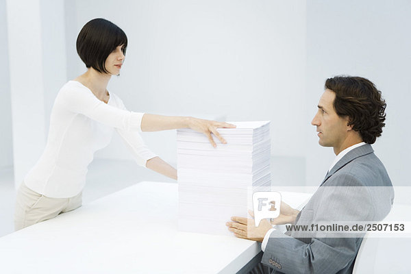 Professionelle Frau und Geschäftsmann tauschen hohen Papierstapel über dem Schreibtisch aus.