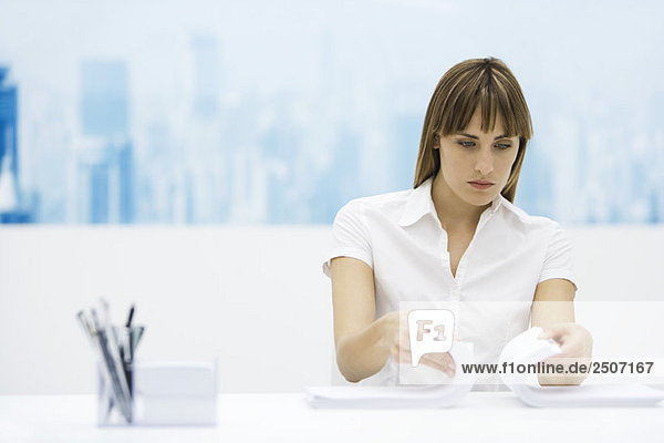 Frau  die zwei Stapel Papier zusammenmischt und am Schreibtisch sitzt.