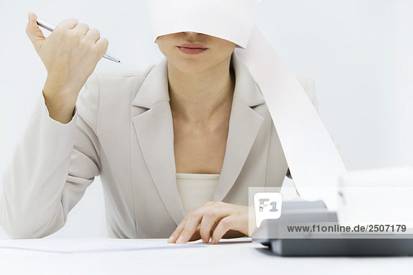 Frau am Schreibtisch sitzend mit um den Kopf gewickeltem Maschinenband  klickender Stift