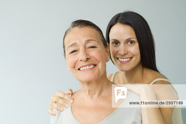Frau hinter älterer Mutter  Hände auf den Schultern  beide lächelnd in die Kamera  Porträt