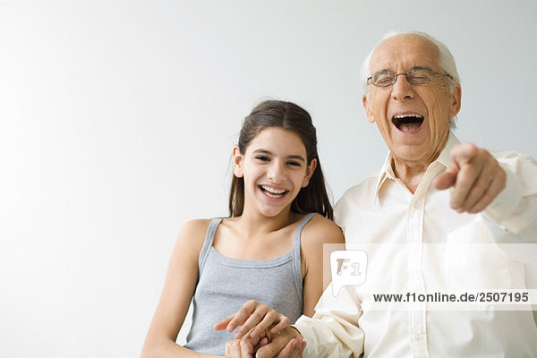 Teenagermädchen Seite an Seite mit Großvater  beide lachend  älterer Mann auf Kamera zeigend