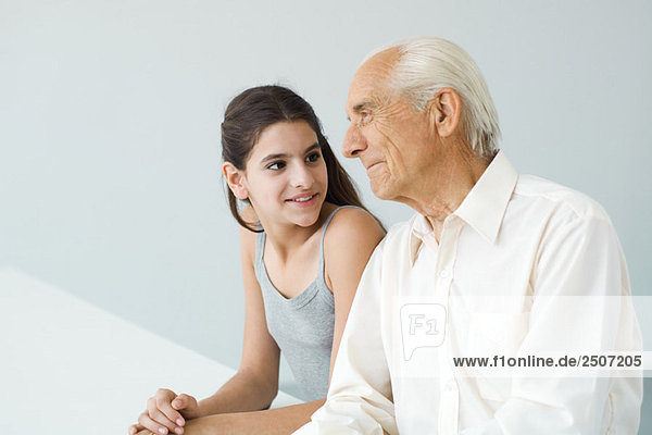 Teenagermädchen schaut Großvater an  Mann schaut weg  beide lächelnd