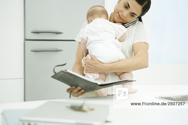 Woman holding baby  using cell phone and looking at agenda