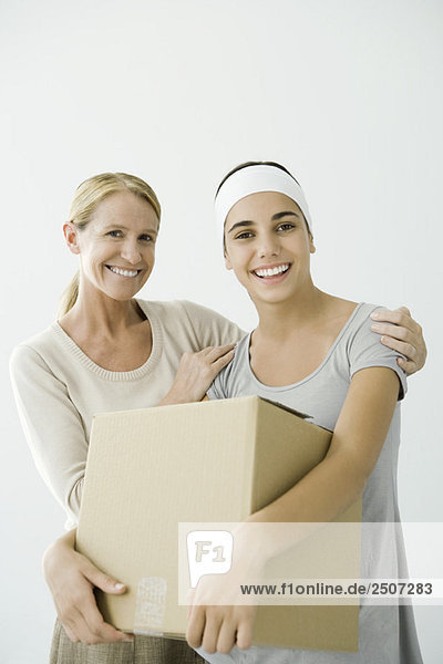 Young female holding cardboard box  mother holding her shoulders