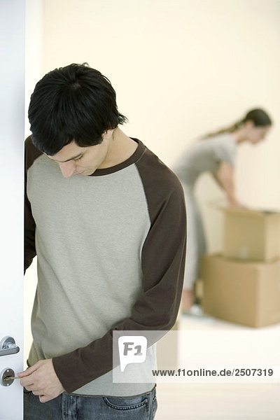 Man testing key on door lock  woman unpacking boxes in background