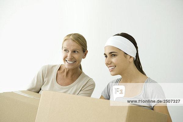 Mother and daughter holding cardboard boxes  both smiling and looking away