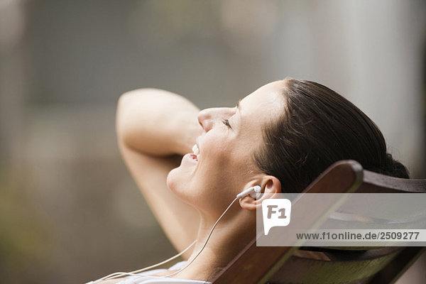 Junge Frau im Liegestuhl beim Hören des MP3-Players  Portrait