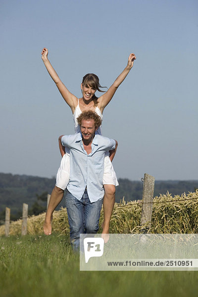 Man giving woman piggyback in meadow  laughing