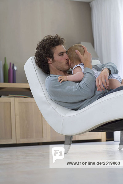 Father kisses baby  sits in chair