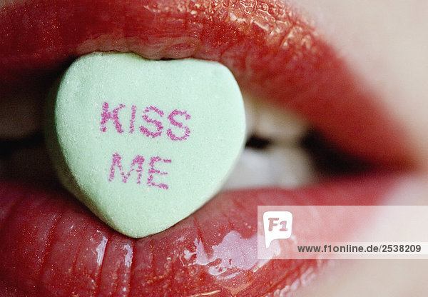 'Close Up of Candy Heart with Words ''Kiss Me'' between Red Lips'