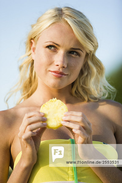 Portrait of a young blond woman eating pineapple slice