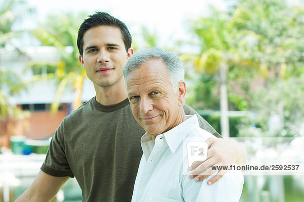 Adult grandson with arm around grandfather  outdoors