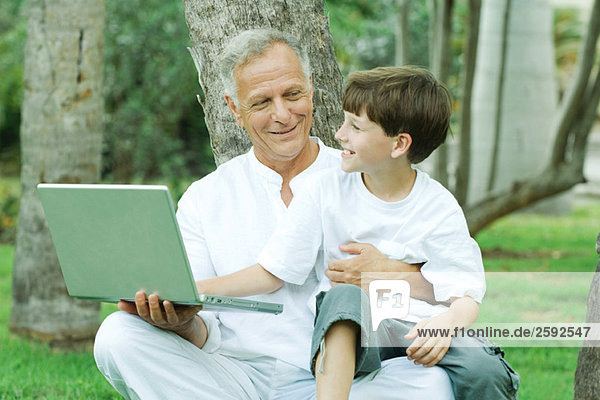 Grandfather holding grandson on lap  boy looking at laptop computer  both smiling