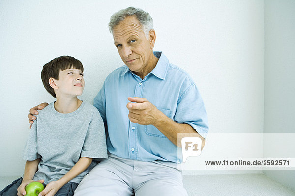 Senior man sitting with grandson  his arm around his shoulder