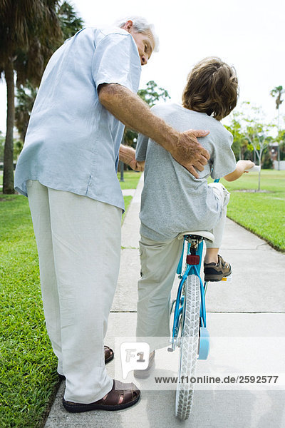 Älterer Mann  der seinem Enkel hilft  Fahrrad fahren zu lernen.