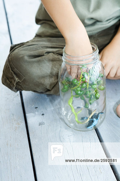 Boy putting berries and toy frog into glass jar  close-up