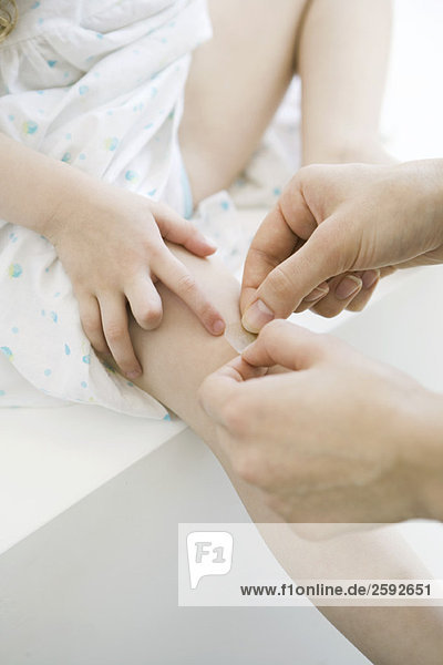 Frau legt Klebebandage auf das Knie des kleinen Mädchens  Schnittansicht