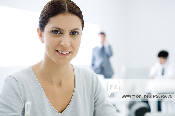 Professional woman smiling at camera  male colleagues in background