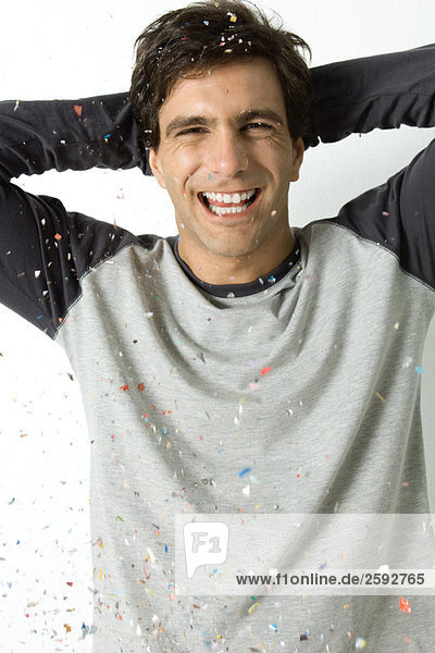 Young man amidst falling confetti  laughing at camera  hands behind head