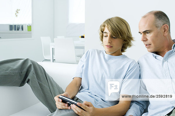 Jugendlicher Junge spielt Handheld-Videospiel  Vater wacht über seine Schulter