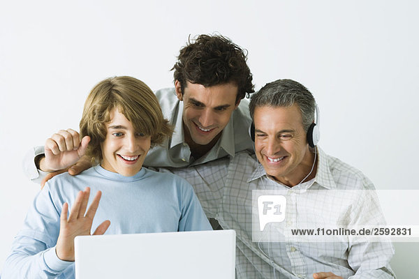 Father and two sons looking at laptop computer together  father wearing headphones