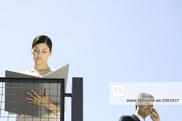 Geschäftsfrau steht im Freien  schaut sich Dokument an  Kollegin mit Handy im Hintergrund