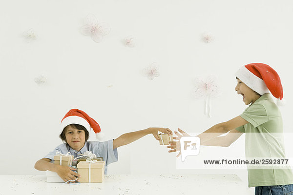 Zwei Jungen mit Weihnachtsmützen stapeln Geschenke  Konfetti fallen um sie herum.