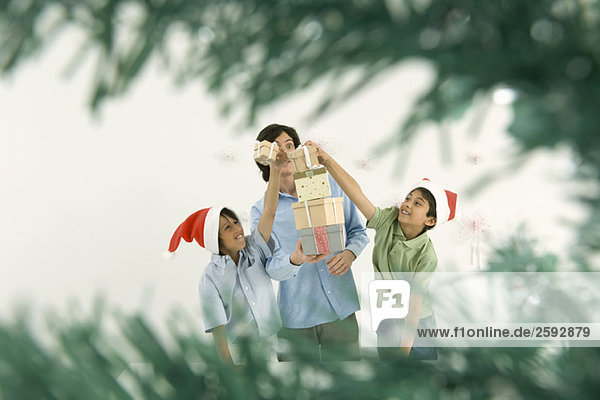 Junger Mann  der einen hohen Stapel Weihnachtsgeschenke hält  Jungen  die mehr Geschenke auf den Stapel legen.